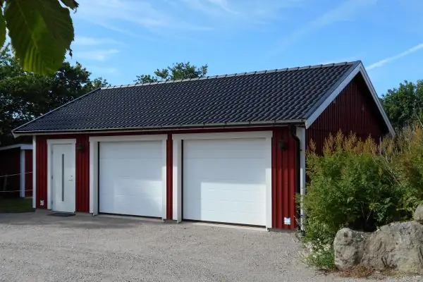 Kunden har valt svarta takpannor. Hängrännor, stuprör och vindskiveplåt är i svart plåt. Portarna är som standard vita men kan även fås i valfri kulör.